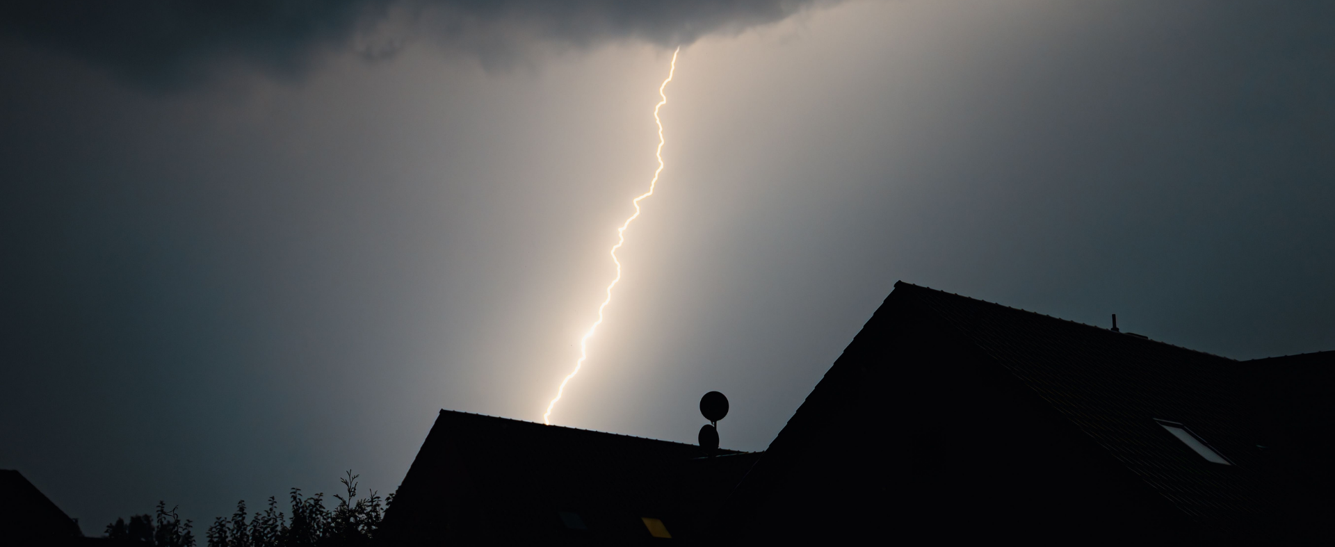 Roof of house with storm and lighting in the background