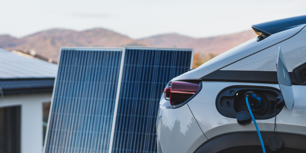 Solar panels next to charging electric vehicle mountain background