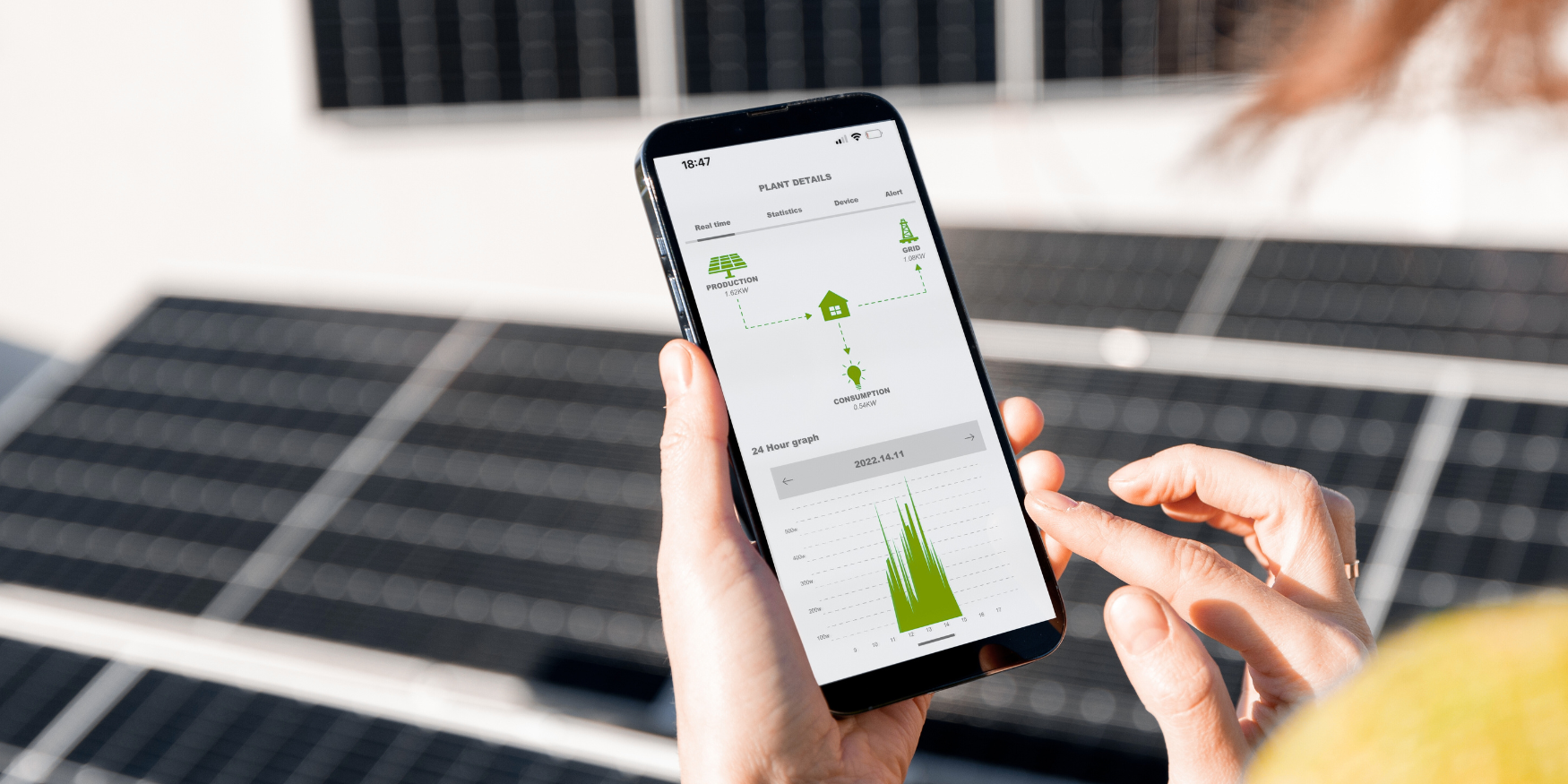 Person monitoring energy usage on phone with solar panels in the background